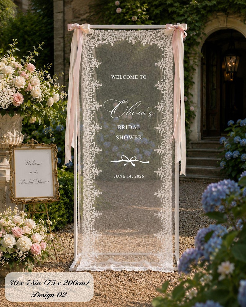 K&ouml;nnte beinhalten: Ein rechteckiger wei&szlig;er Metallrahmen mit einer halbtransparenten wei&szlig;en Spitzenbespannung, bedruckt mit WELCOME TO Olivia's BRIDAL SHOWER JUNE 14, 2026 und einer Schleifengrafik. Der Rahmen ist mit hellrosa B&auml;ndern verziert und misst 75 x 200 cm.