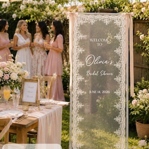 K&ouml;nnte beinhalten: Ein rechteckiges vertikales Schild mit den Ma&szlig;en 75 x 200 cm, bestehend aus einem transparenten wei&szlig;en Stoffpaneel mit aufwendigen Spitzenr&auml;ndern. Das Schild zeigt den Text WELCOME TO Olivia's Bridal Shower JUNE 14, 2026 in wei&szlig;er Schrift.