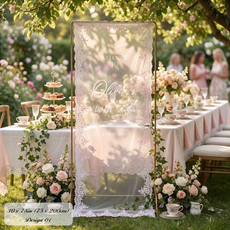 K&ouml;nnte beinhalten: Ein rechteckiges vertikales Schild mit einer transparenten wei&szlig;en Stoffbahn und aufwendigen Spitzenr&auml;ndern, aufgeh&auml;ngt an einem goldfarbenen Metallrahmen. Der Text lautet: WELCOME TO Olivia's Bridal Shower JUNE 14, 2026. Ma&szlig;e: 76 x 198 cm.