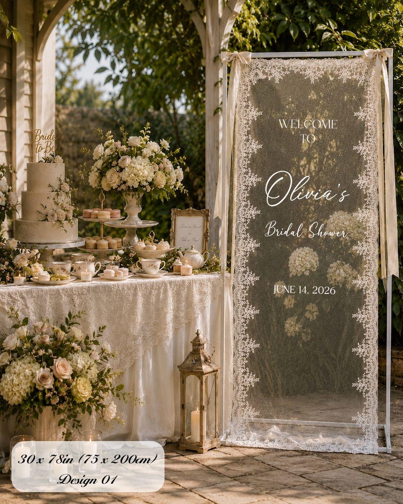 K&ouml;nnte beinhalten: Ein hoher rechteckiger wei&szlig;er Metallrahmen mit einem transparenten Spitzenpaneel, das den Text Welcome to Olivia's Bridal Shower June 14, 2026 tr&auml;gt. Die Spitze hat florale R&auml;nder und misst laut Produktetikett 75 x 200 cm.