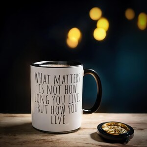 May include: White coffee mug with black text that reads "What matters is not how long you live, but how you live".