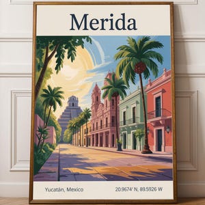 Op de afbeelding: Een ingelijste kunstdruk met een levendige straatscène in Mérida, Mexico. Het kunstwerk toont kleurrijke gebouwen, palmbomen en een piramide op de achtergrond. De print bevat de stadsnaam, locatie en coördinaten.