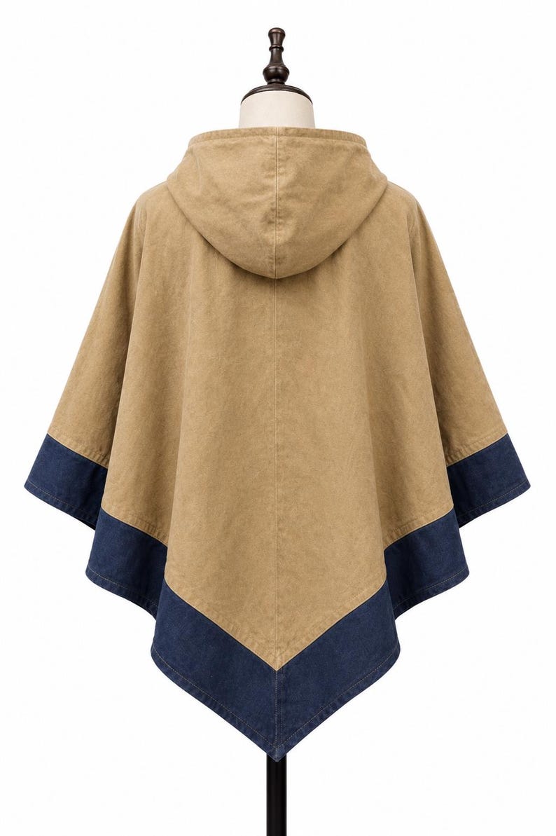May include: A tan hooded poncho with a dark blue denim trim along the bottom edge. The garment is displayed on a mannequin, highlighting its design and shape. The back view shows the hood and the overall silhouette.
