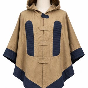 May include: A tan hooded poncho with navy blue detailing. The poncho has a hood, three toggle fastenings, and navy blue quilted panels on the front. The edges are trimmed with navy blue fabric. This outerwear is suitable for various weather conditions.