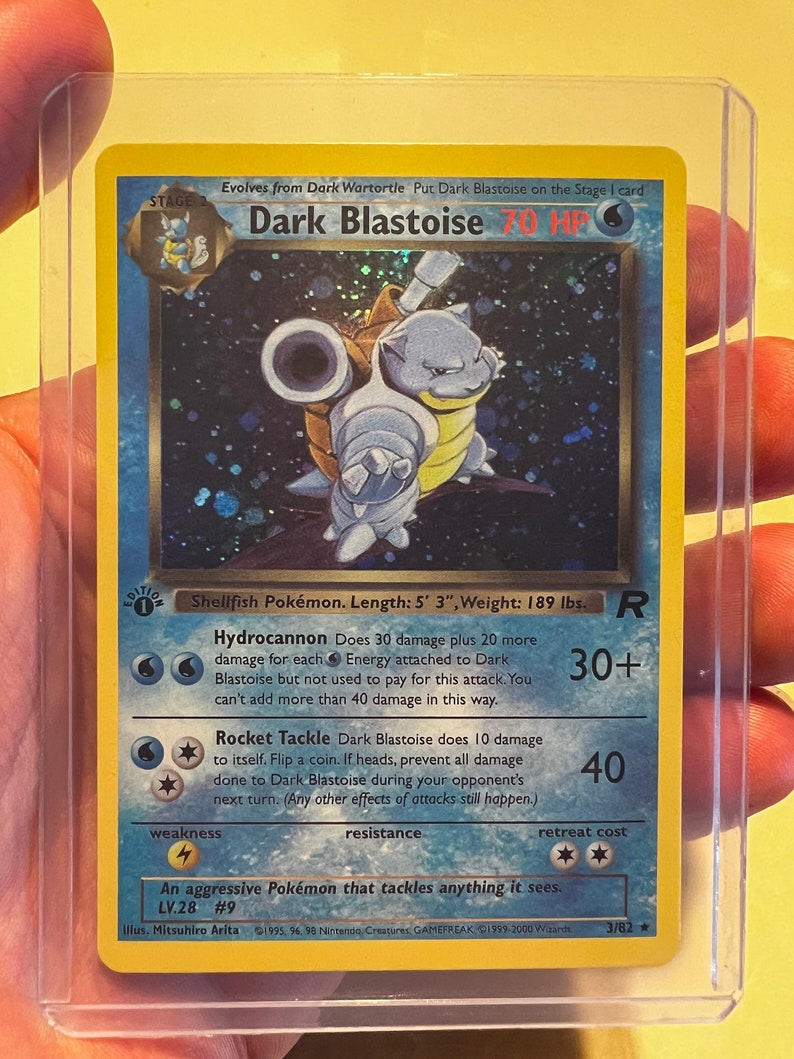 May include: A blue and yellow Pokemon trading card featuring Dark Blastoise, a water-type Pokemon. The card has a blue background with white stars and the text "Dark Blastoise" in large, bold letters. The card also features the Pokemon's stats, including its HP, attack, and retreat cost.