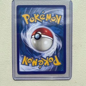 May include: A blue, white, and red Pokemon card back with the word "Pokemon" in white letters and a Pokeball in the center.