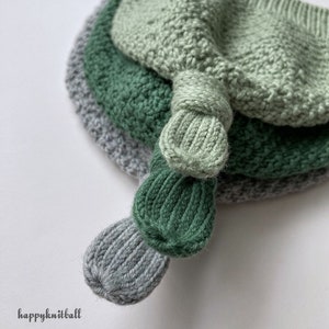 May include: A stack of three knitted hats in light green, dark green, and grey, each featuring a ribbed knot detail at the top. The hats are layered on top of each other, and the text happyknitball is printed in the lower left corner.