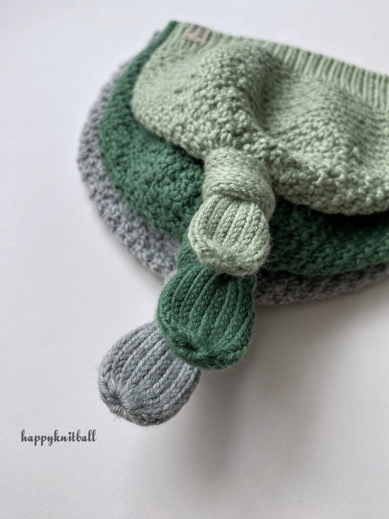 May include: A stack of three knitted hats in light green, dark green, and grey, each featuring a ribbed knot detail at the top. The hats are layered on top of each other, and the text happyknitball is printed in the lower left corner.