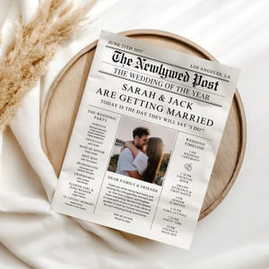 Op de afbeelding: Een huwelijksaankondiging in krantenstijl, getiteld "The Newlywed Post", met de kop "Sarah & Jack gaan trouwen". Het bevat een foto van het paar, huwelijksdetails en een tijdlijn. Het ligt op een houten dienblad.