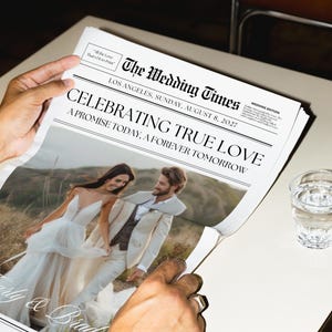 Op de afbeelding: Een krant getiteld "The Wedding Times" met de kop "Celebrating True Love". De afbeelding toont een stel in trouwkleding. De krant wordt door een persoon vastgehouden. Een glas water staat op tafel.