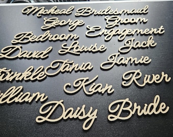 May include: Wooden laser-cut words in a cursive font, including names and event-related terms like "Bride" and "Groom." The words are light-colored against a dark background, ideal for wedding decor or personalized gifts.