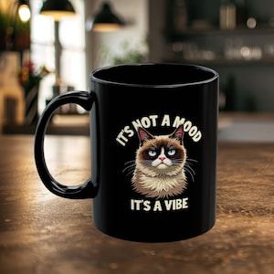 May include: Black coffee mug with a grumpy cat illustration and the text "It's not a mood, it's a vibe".