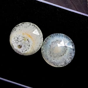 Può includere: Due pietre di agata rotonde e lucide. Una pietra ha un motivo bianco, nero e giallo, mentre l'altra è blu pallido e bianco. Entrambe le pietre hanno un taglio geometrico sfaccettato sulla superficie.