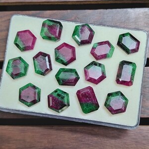 May include: A collection of faceted gemstones with a mix of shapes, including hexagons and rectangles. The gems feature a vibrant combination of deep red and green hues, displayed in a clear plastic case against a neutral background. The gemstones are likely for jewelry making.