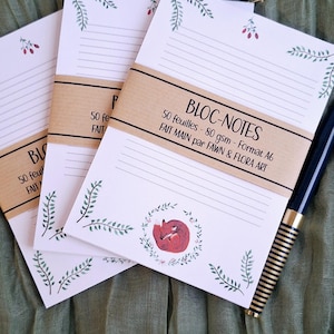 May include: Three notepads with lined pages and a brown paper band. The top notepad has the text "BLOC-NOTES" and "FAIT MAIN par FAWN & FLORA ART". Each notepad has a botanical illustration and a pen.