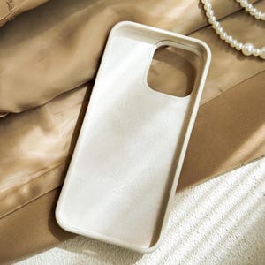 a white case sitting on top of a bed next to a pearl necklace