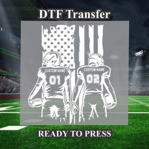 May include: White DTF transfer featuring two football players with the American flag in the background. The text "CUSTOM NAME" appears above each player's jersey number. The text "READY TO PRESS" is at the bottom.