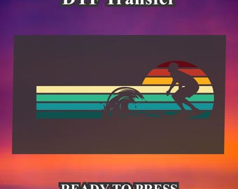 May include: A silhouette of a person surfing a wave with a sunset background. The image has a retro, vintage aesthetic with a colorful striped design. The text "DTF Transfer" and "READY TO PRESS" is included in the image.
