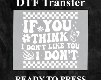 Puede incluir: Transferencia termoadhesiva blanca con el texto "IF YOU *THINK I DON'T LIKE YOU I DON'T" en una fuente retro sobre un fondo a cuadros con una mariposa, una flor y un gráfico de mano. También se incluyen los textos "DTF Transfer" y "READY TO PRESS".