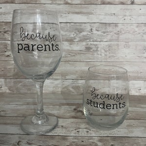 May include: Two clear glass wine glasses with black lettering. The larger glass says "because parents." The smaller glass says "because students."
