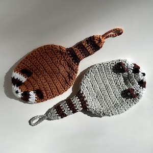 Può includere: Due giocattoli di animali all'uncinetto con code lunghe. Uno è marrone e bianco con il naso rosso e l'altro è grigio e marrone.