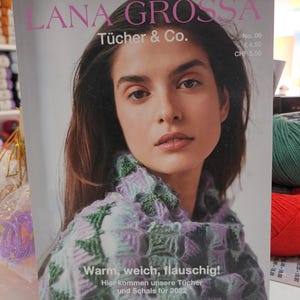 Könnte beinhalten: Ein Magazincover mit einer Frau, die einen bunten Strick Schal trägt. Das Magazin heißt "Lana Grossa Tücher & Co." und der Text "Warm, weich, flauschig! Hier kommen unsere Tücher und Schals für 2022" ist unten aufgedruckt.