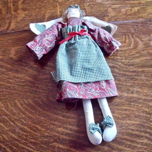 May include: A handmade rag doll angel with a green and white plaid dress, red ribbon, and paisley print skirt. The doll has a white fabric halo and wings.