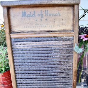 May include: A vintage wooden washboard with a metal grate. The washboard has a sign that reads "Maid of Honor" with the words "Sold Only By Sears, Roebuck and Co."