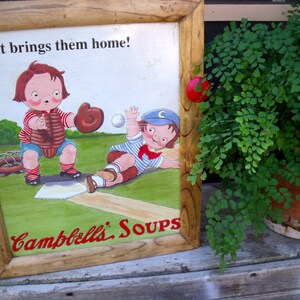 May include: A vintage wooden framed sign with a colorful illustration of two children playing baseball. The sign reads "It brings them home! Campbell's Soups".