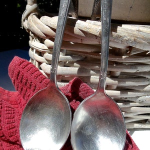 May include: Two silver spoons with ornate handles, resting on a red knitted fabric. The spoons are polished and reflect light.