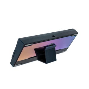 May include: A black electronic device with a color-shifting screen, supported by a matching stand. The screen displays a gradient of purple, orange, and blue hues. The device has a sleek, modern design.