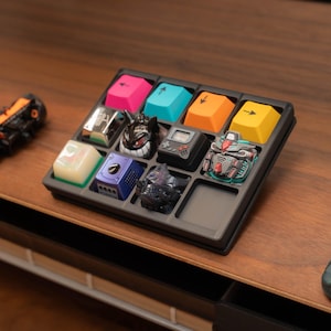 以下が含まれることがあります： カスタムメカニカルキーボードのキーキャップのトレイ。キーキャップは、ピンク、ティール、オレンジ、黄色の矢印キーなど、さまざまな色とデザインがあります。他のキーキャップは、笑顔の漫画のキャラクターやロボットなど、ユニークなデザインが特徴です。