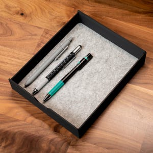 May include: Three pens in a black felt-lined tray. The pens are a silver pen with a black clip, a black pen with a silver clip and a ruler, and a black pen with a turquoise barrel and a silver clip.