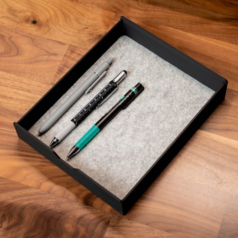 May include: Three pens in a black felt-lined tray. The pens are a silver pen with a black clip, a black pen with a silver clip and a ruler, and a black pen with a turquoise barrel and a silver clip.