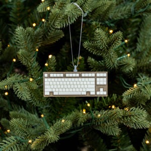 Puede incluir: Un adorno de teclado de computadora blanco colgando de una cuerda blanca en un árbol de Navidad verde.
