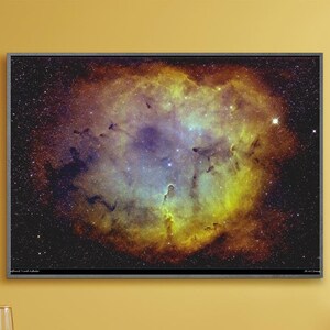 May include: A framed photograph of a nebula in space, with a dark background and a bright, colorful nebula in the center. The nebula is a mix of yellow, orange, red, and blue colors.