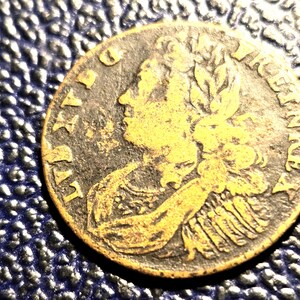 May include: A close-up of an antique coin with a profile of a person on the obverse. The coin has a gold and bronze color with visible text around the edges. The coin is set against a textured blue background.