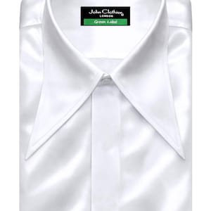 Puede incluir: Camisa blanca impecable, cuidadosamente doblada. Presenta un cuello puntiagudo y una etiqueta « John Clothier London Green Label ». El tejido brillante sugiere un material de calidad, ideal para ocasiones formales.