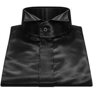 Könnte beinhalten: Ein gefaltetes schwarzes Satinhemd mit klassischem Kragen und einem einzelnen Knopfverschluss. Das Hemd hat eine glatte, glänzende Oberfläche, und der Stoff scheint elegant zu fallen. Die Gesamtästhetik ist schlicht und elegant.