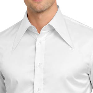 Può includere: Primo piano di una camicia bianca con un ampio colletto a punta. La camicia è abbottonata e il tessuto appare liscio. Il colletto è una caratteristica importante, che crea un'estetica retrò o vintage.