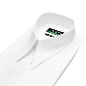 May include: A crisp white long-sleeve dress shirt featuring a sharp, pointed collar. Inside the collar, a black label displays the text John Clothier London, Green Label, and 100% Cotton. The shirt is folded neatly, highlighting the structured collar.