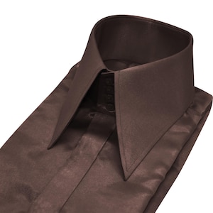 Peut inclure: Chemise marron pliée avec un col haut et pointu. La chemise est faite d'une matière lisse, semblable à du satin, et possède une fermeture à boutons sur le devant. Le col est d'une nuance de marron plus foncée que le reste de la chemise.
