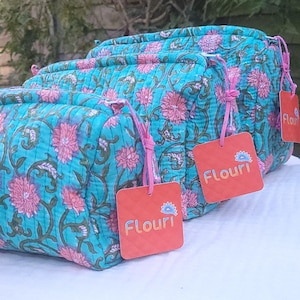 Può includere: Tre trousse da trucco trapuntate di colore turchese con motivi floreali rosa e nappine rosa. Ogni trousse ha un'etichetta quadrata rossa con la parola "Flouri" stampata su di essa.