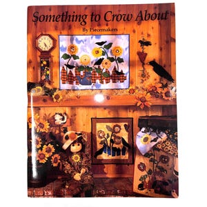 May include: A book cover titled "Something to Crow About" by Piecemakers. The cover features a wooden background with a clock, sunflowers, and a quilt with sunflowers and crows. A doll and other decorative items are also visible.