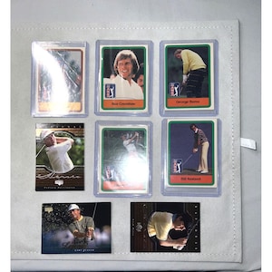 Puede incluir: Una colección de tarjetas de golf vintage, cada una en una funda protectora. Las tarjetas muestran a golfistas en acción y retratos, incluyendo a Ben Crenshaw y George Burns. Las tarjetas se muestran sobre una superficie blanca.