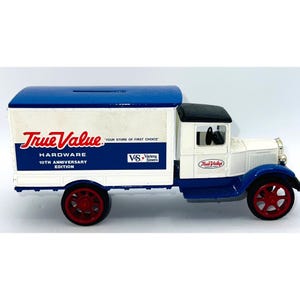 May include: A die-cast metal toy delivery truck featuring a white cab and a blue cargo box with a coin slot on top. The side displays True Value Hardware 10th Anniversary Edition branding with red wheels, a black roof, and white and blue paint.