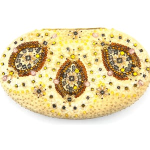 Könnte beinhalten: Cremefarbene ovale Clutch mit aufwendiger Perlenarbeit. Das Perlendesign zeigt drei große, ovale Muster in Braun-, Gelb- und Grautönen, umgeben von kleineren Blumen- und Sternmustern. Die Clutch ist mit kleinen, goldfarbenen Perlen verziert.