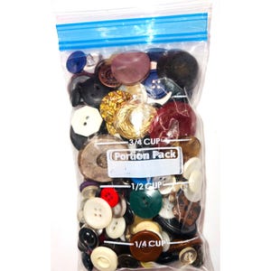 May include: A clear plastic resealable bag filled with a variety of assorted buttons in different colors, shapes, and sizes. The bag features printed white measurement markings for 1/4 cup, 1/2 cup, and 3/4 cup, along with the text Portion Pack.