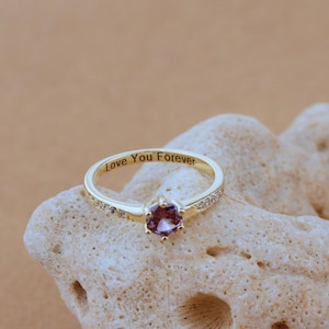 Könnte beinhalten: Ein goldener Ring mit einem kleinen rosafarbenen Edelstein und einer Reihe kleiner, klarer Steine. Die Innenseite des Rings ist mit den Worten "Love You Forever" graviert.