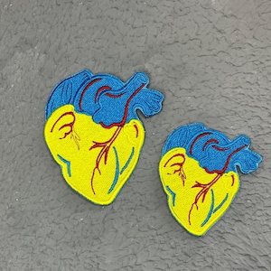 May include: Two embroidered iron-on patches in the shape of a heart. The larger patch is yellow with a blue outline and the smaller patch is yellow with a blue outline. Both patches have red stitching.